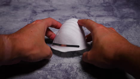men's hands first person view taking and putting protective face mask on camera white mask from threat like corona covid-19 virus protects mouth and nose from dark black board capture in 4k 60fps