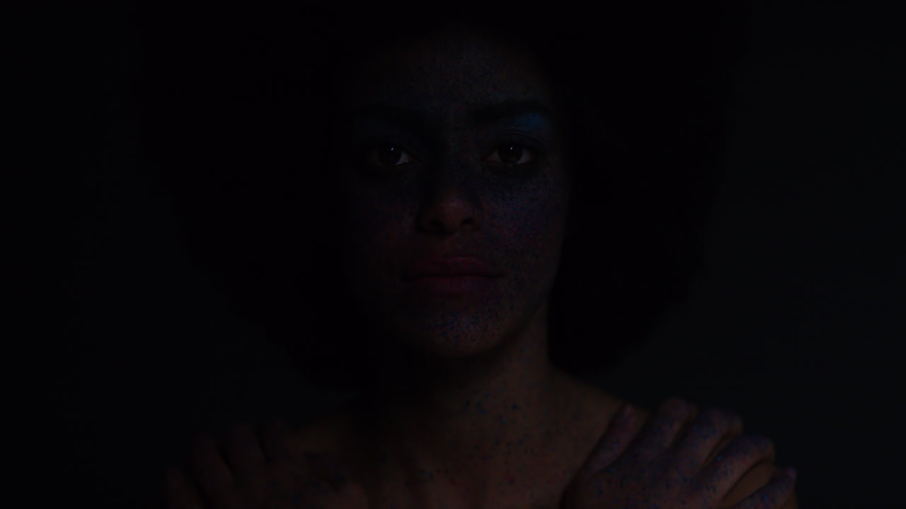 retrato de una hermosa mujer afroamericana con rostro exótico, pintura corporal, arte corporal, mujer misteriosa con maquillaje colorido, luz parpadeando en un fondo oscuro, concepto de expresión creativa