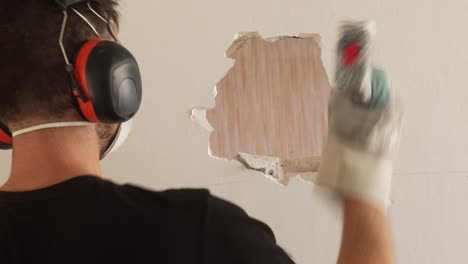 Male-contractor-punching-a-hole-in-white-wall-with-sledge-hammer,-medium-static-shot