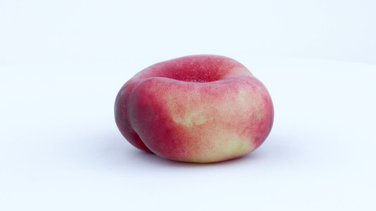 En hel doughnut-formet flad fersken kaldet Saturn. Roterende på en drejeskive, isoleret på hvid baggrund. Nærbillede. Makro