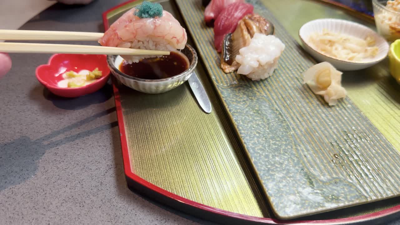 Detailní záběr osoby, která namáčí krevetové suši do sójové omáčky na elegantním podnosu v restauraci