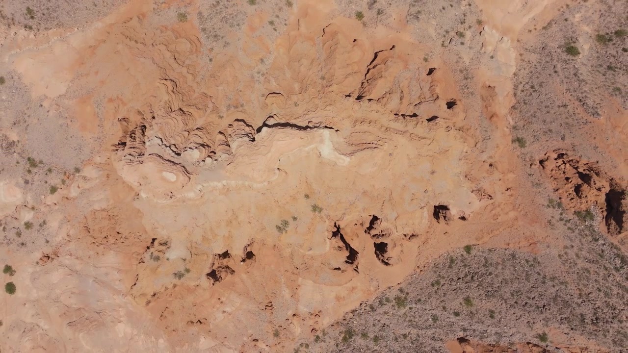 Ripresa aerea con drone di formazioni di arenaria stratificate e terreno desertico eroso, ascesa per rivelare il paesaggio.