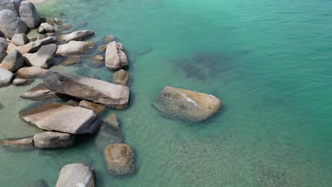 flying over calm waters with big rocks on the left side of the frame