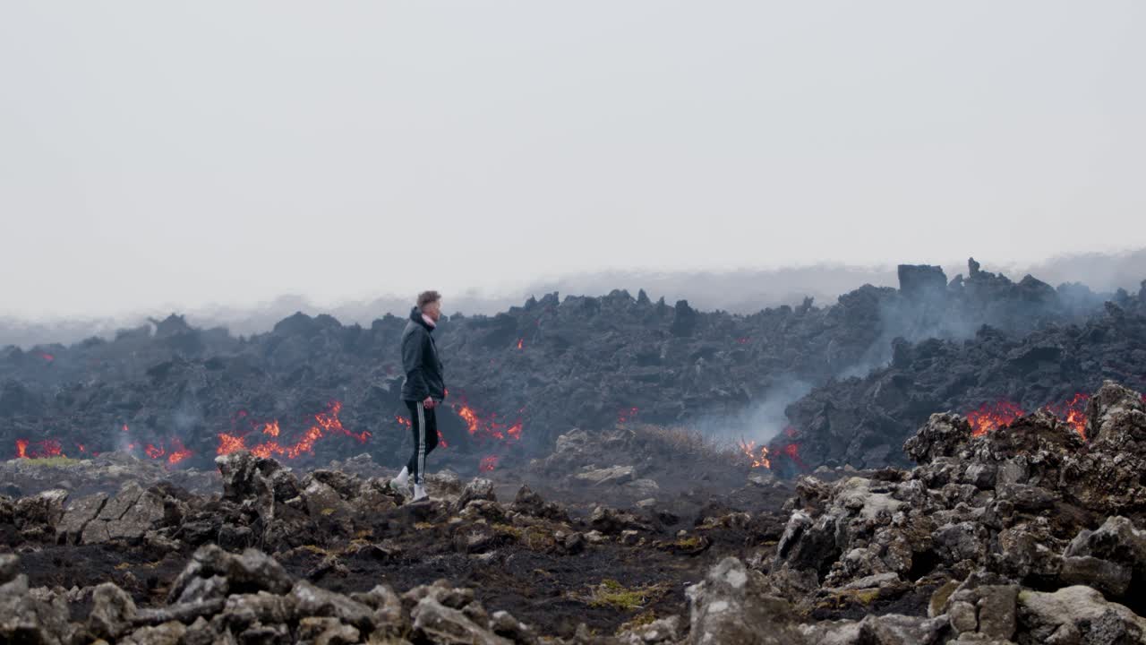 hombre caminando a través de un paisaje rocoso cerca del flujo de lava derretida en el volcán grindavik, islandia