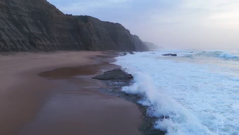 Luftaufnahme-über-Den-Wellen-Am-Strand-Von-Magoito,-Bewölkter-Sonnenuntergang-In-Portugal