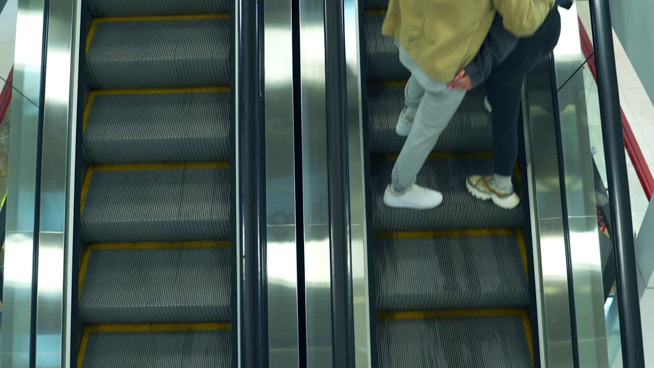 Metal escalator stairs moving in both directions up and down. Young couple standing on the steps, embracing and going up. Top view.