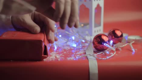 wrapping christmas gift with ribbons and red paper with red background and baubles