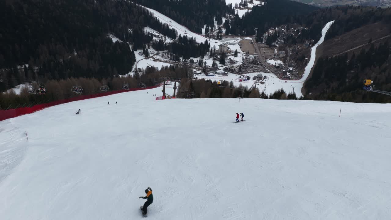 Riprese aeree con drone che mostrano una fluida ripresa a seguire di uno snowboarder che scende una pista da sci a Folgaria, Italia, evidenziando velocità e azione dinamica invernale.