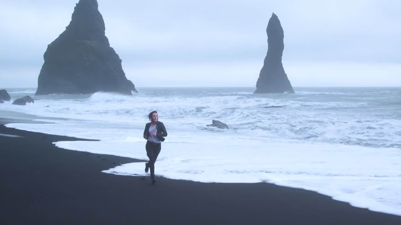 Gloomy Icelandic beach landscape with woman running. Aerial flying backwards