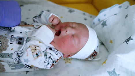 gloved hands are fastening the buttons on baby's romper. newborn kid starts to cry. close up.