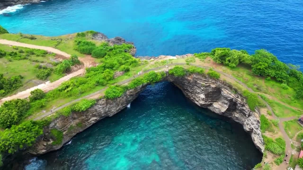 Aerial drone flying over and on top of Bali Broken beach shoreline with cliffs, blue ocean and a large ground hole or cavity that is filled with ocean sea water during a sunny day. White water waves.
