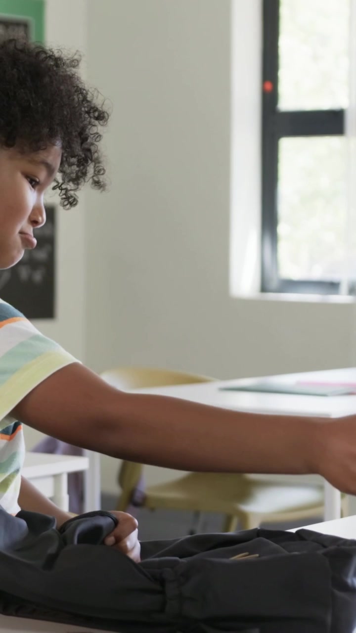 Vertical video: Striped student opening backpack, getting tablet and passing at desk, copy space