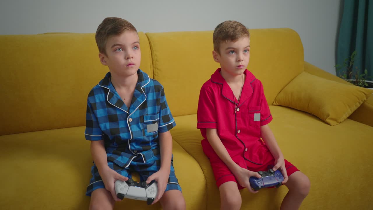 To drenge, der spiller videospil på en gul sofa