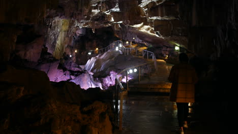 a woman walking along a pathway inside a cavern with rugged rock formations illuminated by colorful lights