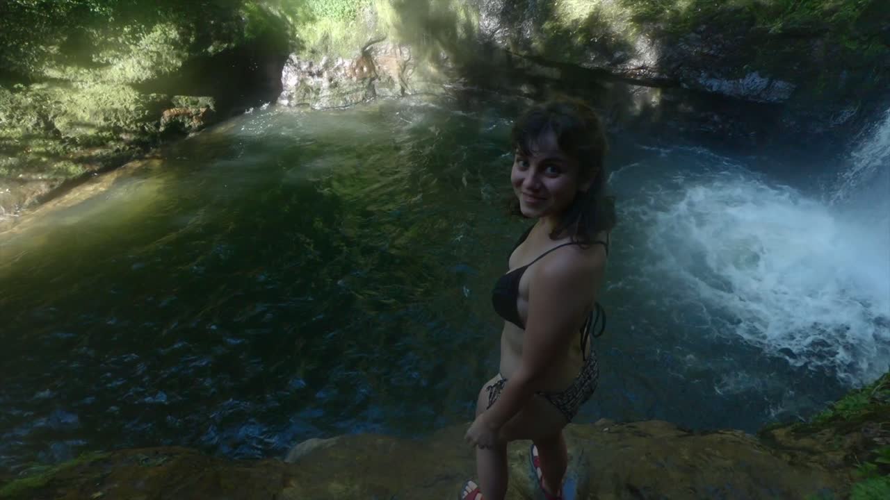 Woman in bikini jumping off a cliff near a waterfall