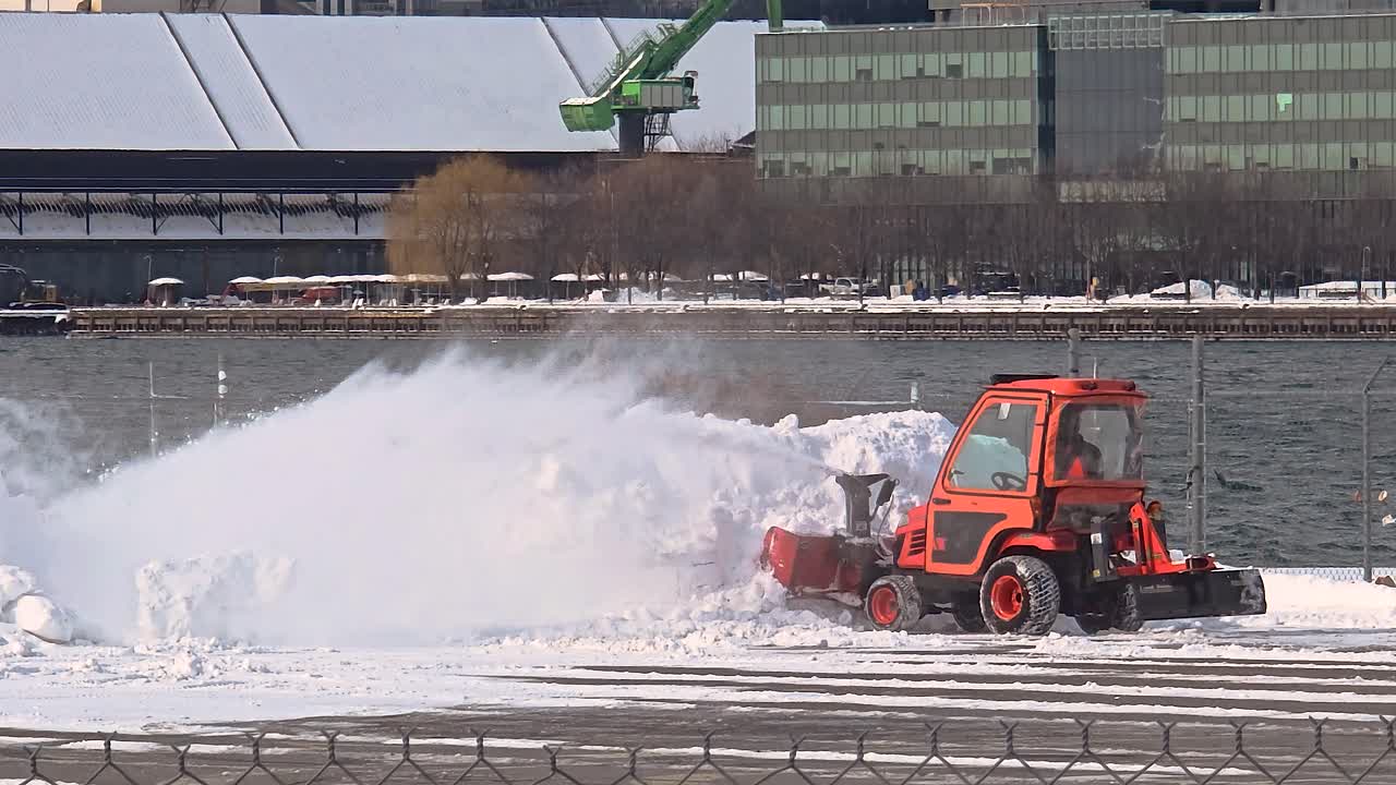 Snow blower clears industrial site near harbor on cold winter day