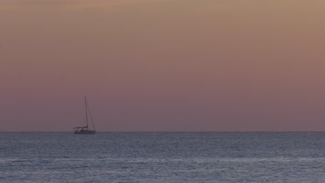 small sailing yacht at dawn heading out to sea, sails furled