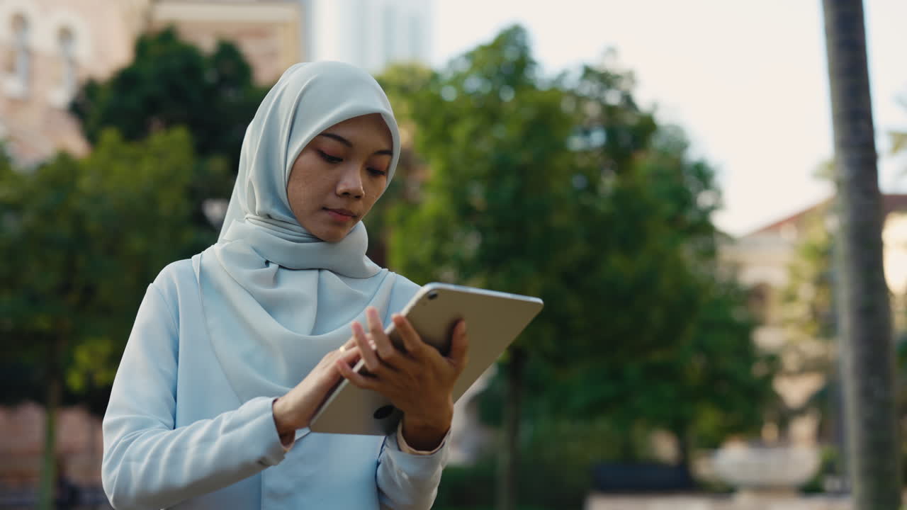 Young woman in hijab using a tablet outdoors