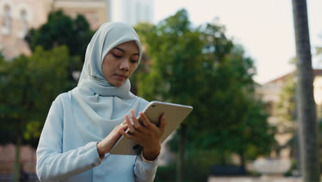 young woman in hijab using a tablet outdoors