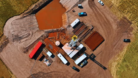 drone flying above the location for drilling the natural resources. trucks, pipes, metal rig and pools with dirty water from aerial perspective.