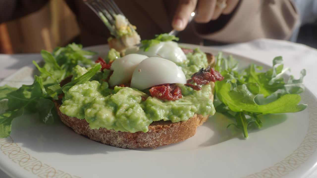 Close-Up of Person Eating Healthy Avocado Toast with Poached Eggs