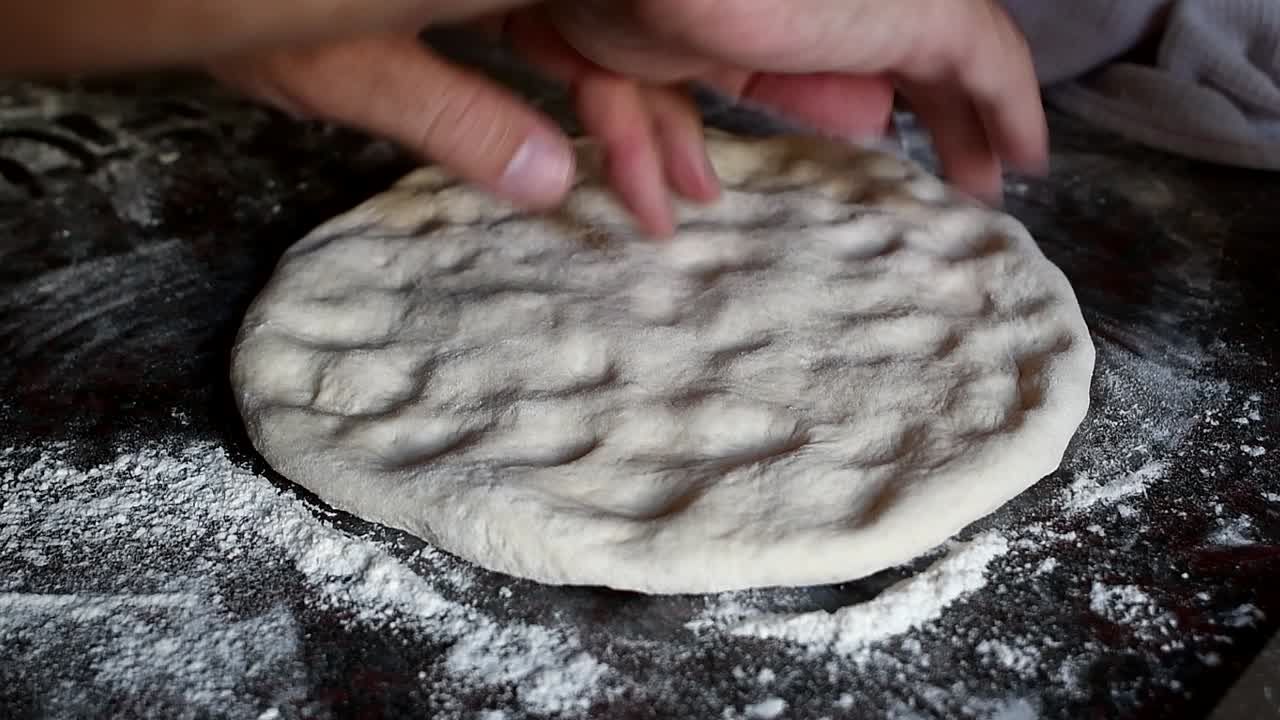 Working on a home made pizza dough with the bare hands on a marble kitchen counter. Side view, medium high angle. Natural window light