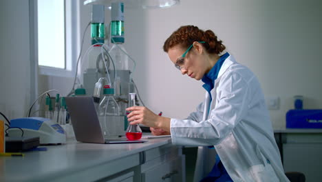 scientist find a cure. woman scientist looking at chemical liquid in lab flask