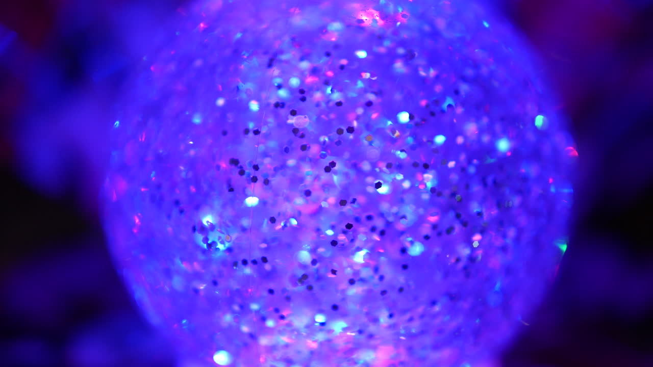 A glowing glitter-filled decorative orb illuminated in purple and blue hues with shimmering particles catching the light