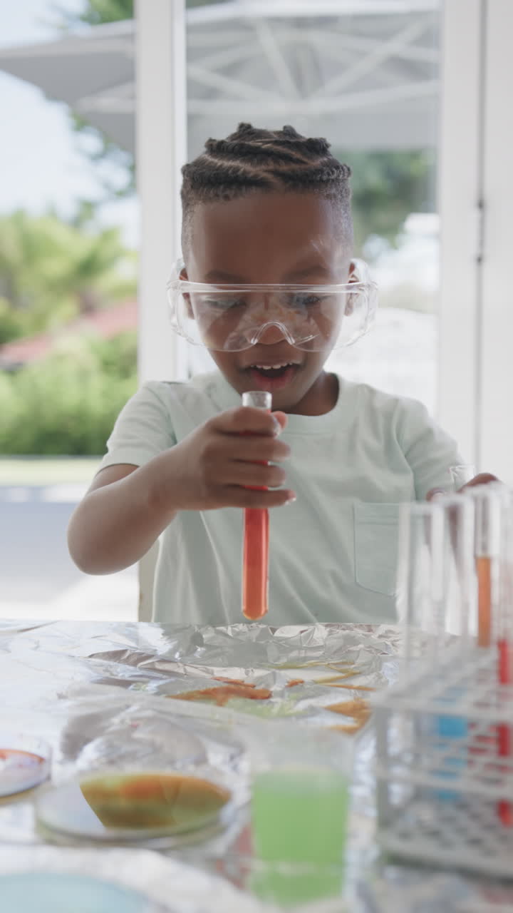 Vertikal video af afroamerikansk dreng, der sidder ved et bord og holder reagensglas med væske, i slowmotion.