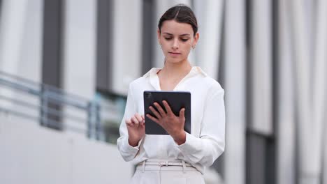 businesswoman walking past a modern building while working on her tablet