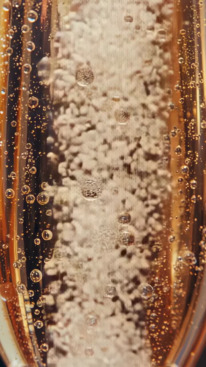 Vertical video: Nucleation points forming bubbles and rising inside glass vessel, golden liquid