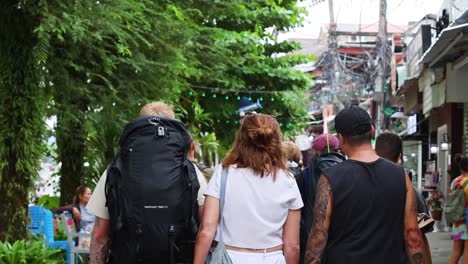 a group of friends walks down a leafy street lined with shops and greenery.