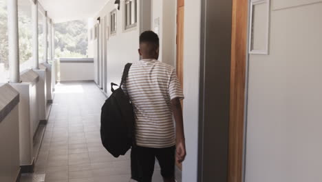 walking down school hallway, african american teenage boy carrying backpack heading to classroom