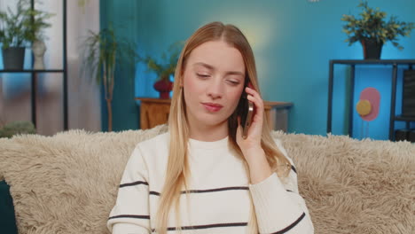 caucasian woman sitting on sofa at home shocked and sad after receiving bad news on smartphone