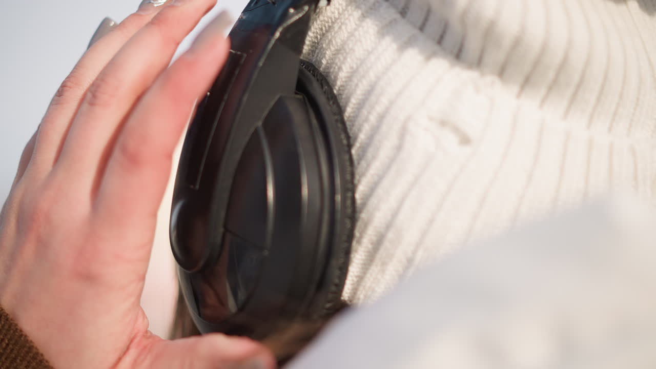 Close up shot of black ear headphone being adjusted by hand wearing knit beanie and puffer jacket, sunlight reflecting off metal accents, highlighting nail art on fingers in crisp winter setting