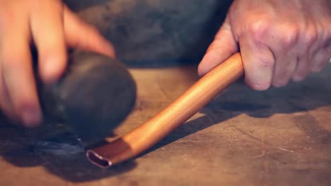 detalle de un hombre martillando un tubo de cobre sobre una mesa