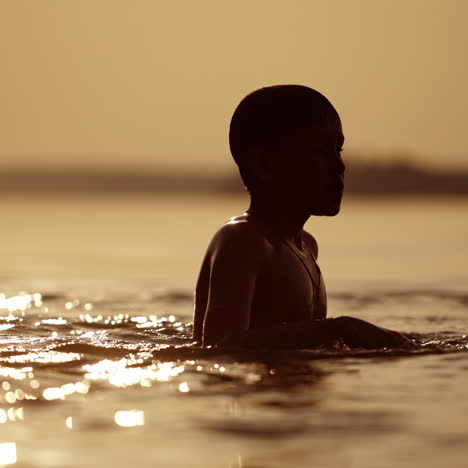 boy swims in the river at sunset. active child dives underwater in the evening. silhouette of a kid swimming to his mother outdoors. close-up.