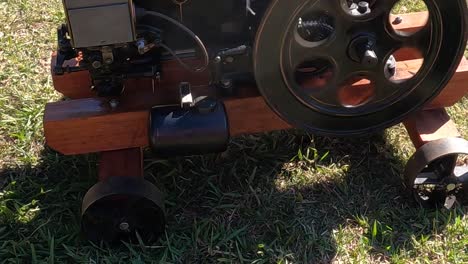 detailed view of a vintage engine wheel and wooden base on a grassy field.