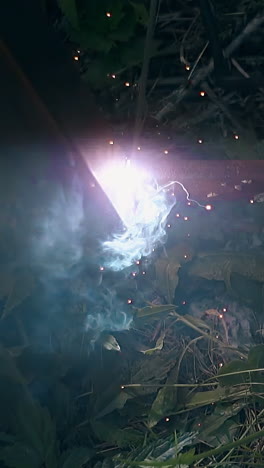 slow motion welding of country house fence bottom parts with smoke and sparks among green leaves