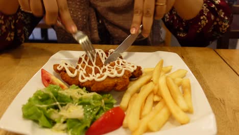 mujer comiendo chuleta de pollo con papas fritas y ensalada