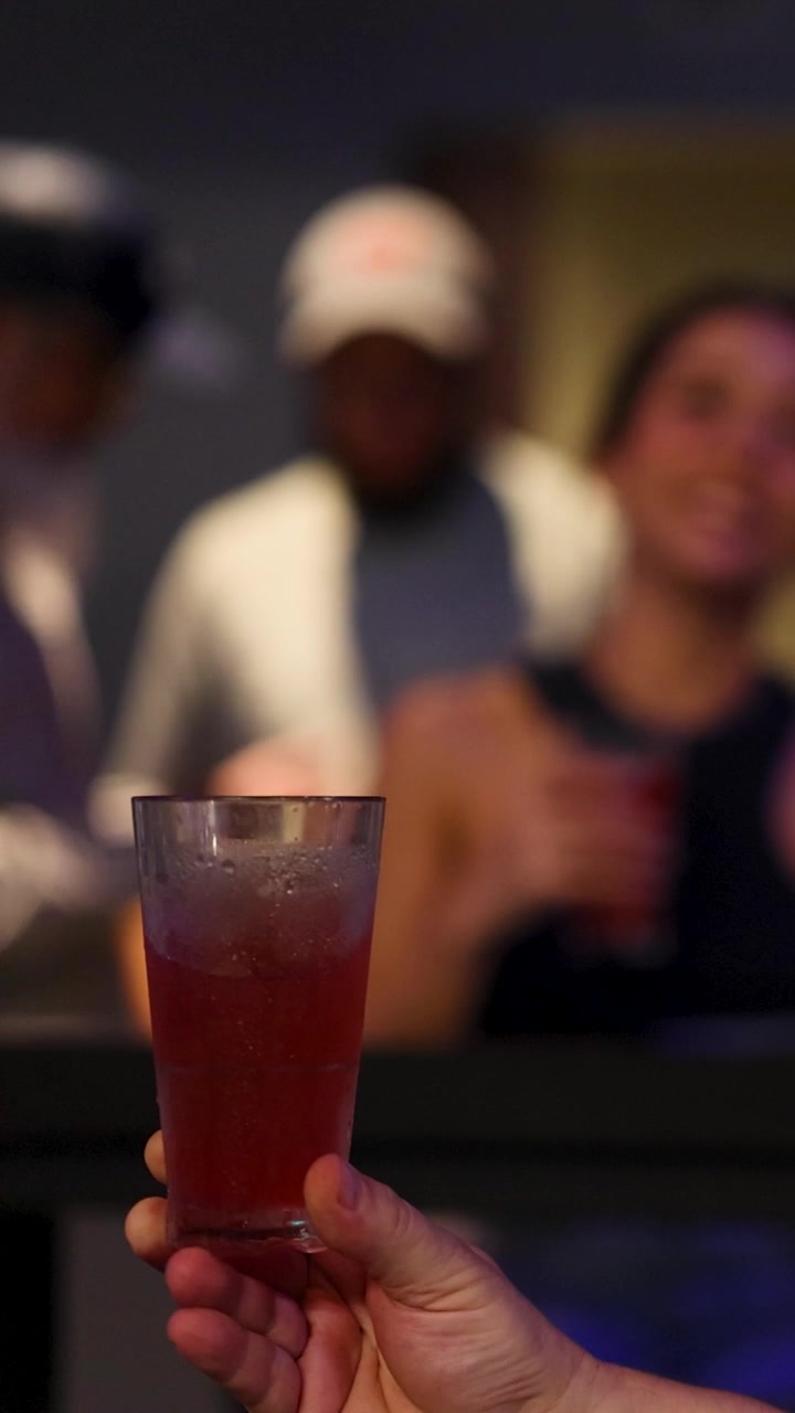 Mano che tiene un cocktail rosso in un ambiente sociale sfocato