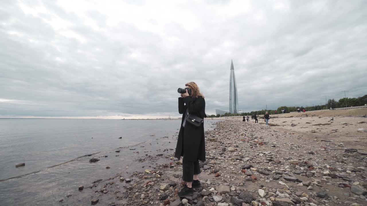 Женщина фотографирует на пляже с видом на небоскребы
