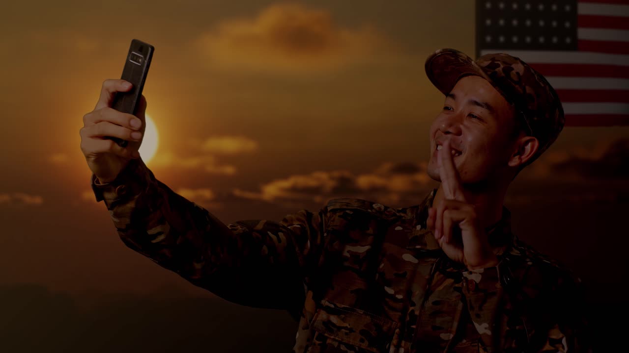 primer plano de un soldado asiático usando un teléfono inteligente tomando una foto mientras está de pie con la bandera de los estados unidos, hora del atardecer