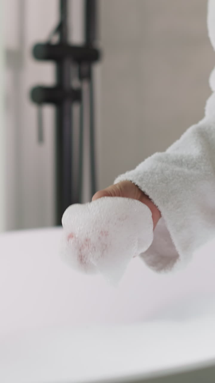 la dama toca la espuma de jabón en el baño jugosamente sentada en el borde de la bañera. la mujer en túnica de baño de terry disfruta de la espuma suave esperando los procedimientos de relajación del spa. ritual de cuidado