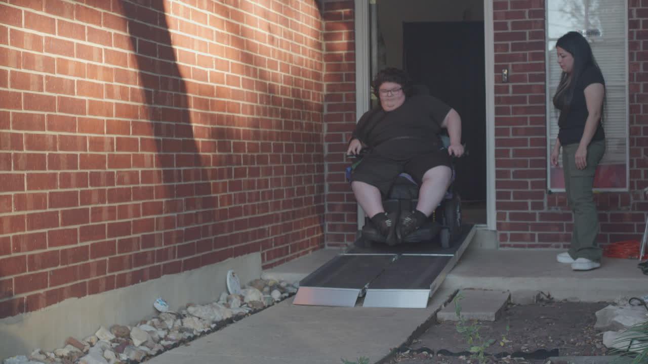 Muscular Dystrophy adolecsent in wheelchair going down ramp monitored by mom