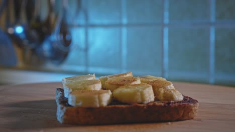 Espolvorear-Canela-En-Polvo-Sobre-Tostadas-Integrales-Con-Mermelada-De-Arándanos,-Mantequilla-De-Maní-Y-Plátano-Como-Refrigerio-Antes-Del-Entrenamiento