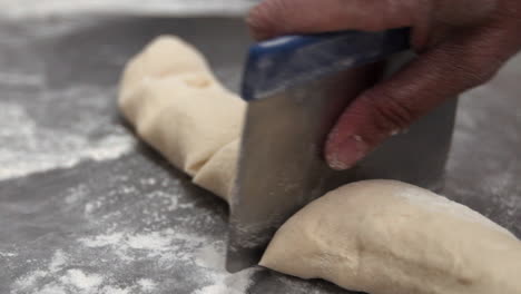 Cutting-a-long-piece-of-dough-with-a-sharp-chef-knife-on-a-stainless-steal-table-to-make-a-pastry
