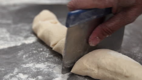 cutting a long piece of dough with a sharp chef knife on a stainless steal table to make a pastry