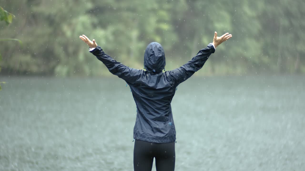 한 여자가 호수의 배경에 비를 내리고 서 있습니다. 슈퍼 슬로 모션 카메라 1000fps로 촬영되었습니다.