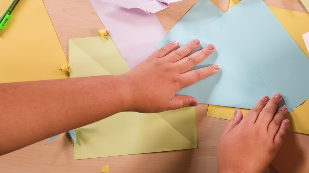 Overhead view of hands carefully folding blue paper during a creative origami craft session